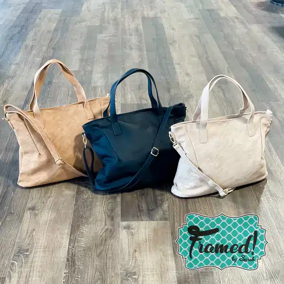 Tan, black, and ivory vegan leather large purses in a row on a wood floor