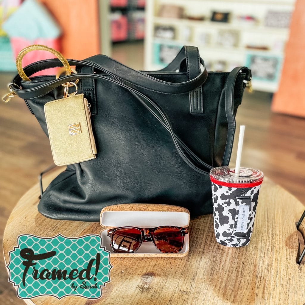 black tote bag on a table with gold wristlet, sunglasses, and tumbler