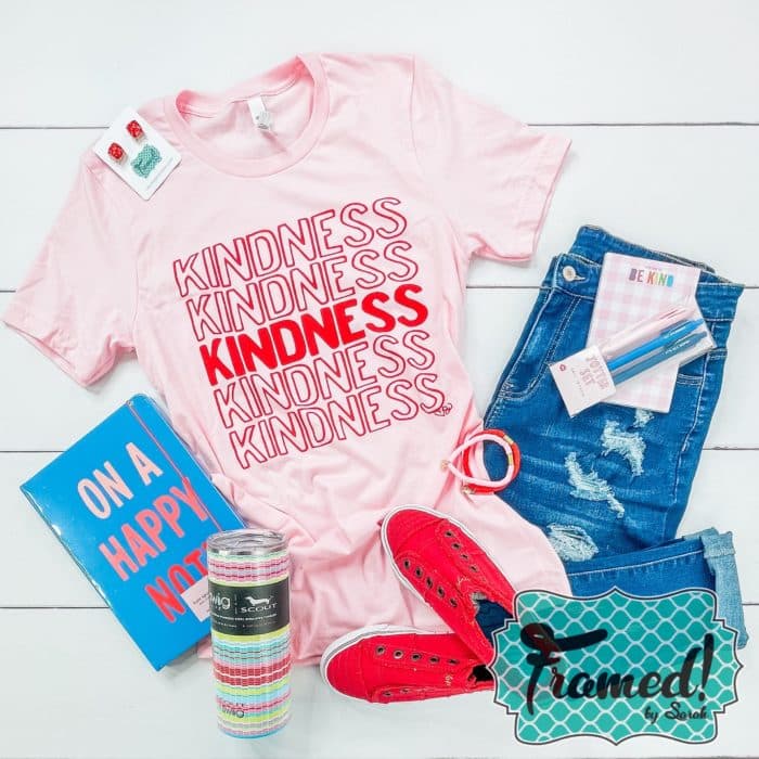 Pink Kindness shirt paired with jeans, red shoes, a notebook and tumbler
