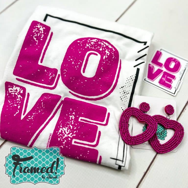 white "love" graphic tee folded on the table with the pink heart beaded earings
