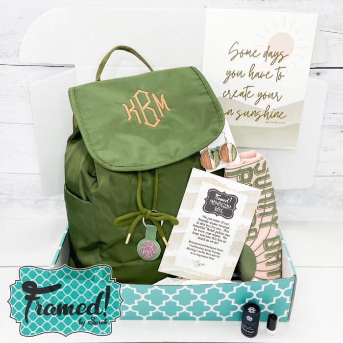 Monogram Box open displaying a green backpack with peach monogram, art print with quote, perfume, tshirt, and earrings.
