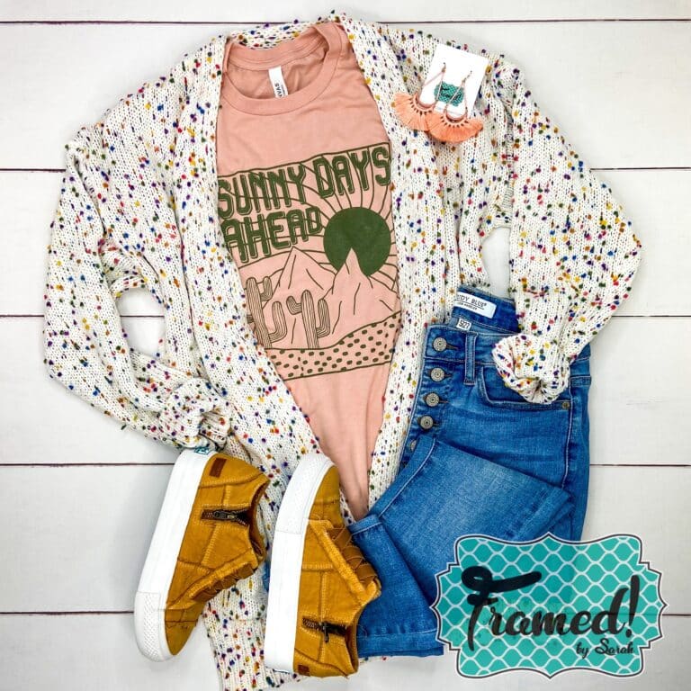 Peach shirt with a desert scene and the word Sunny Days Ahead in olive green ink. Styled with Jeans and camel shoes and white confetti cardigan