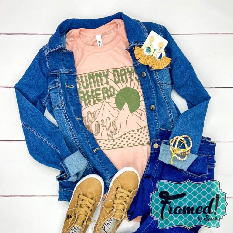 Peach shirt with a desert scene and the word Sunny Days Ahead in olive green ink. Styled with denim jacket and tan accessories