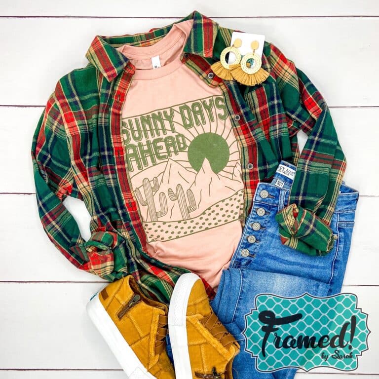 Peach shirt with a desert scene and the word Sunny Days Ahead in olive green ink. Styled with Jeans and green flannel shirt