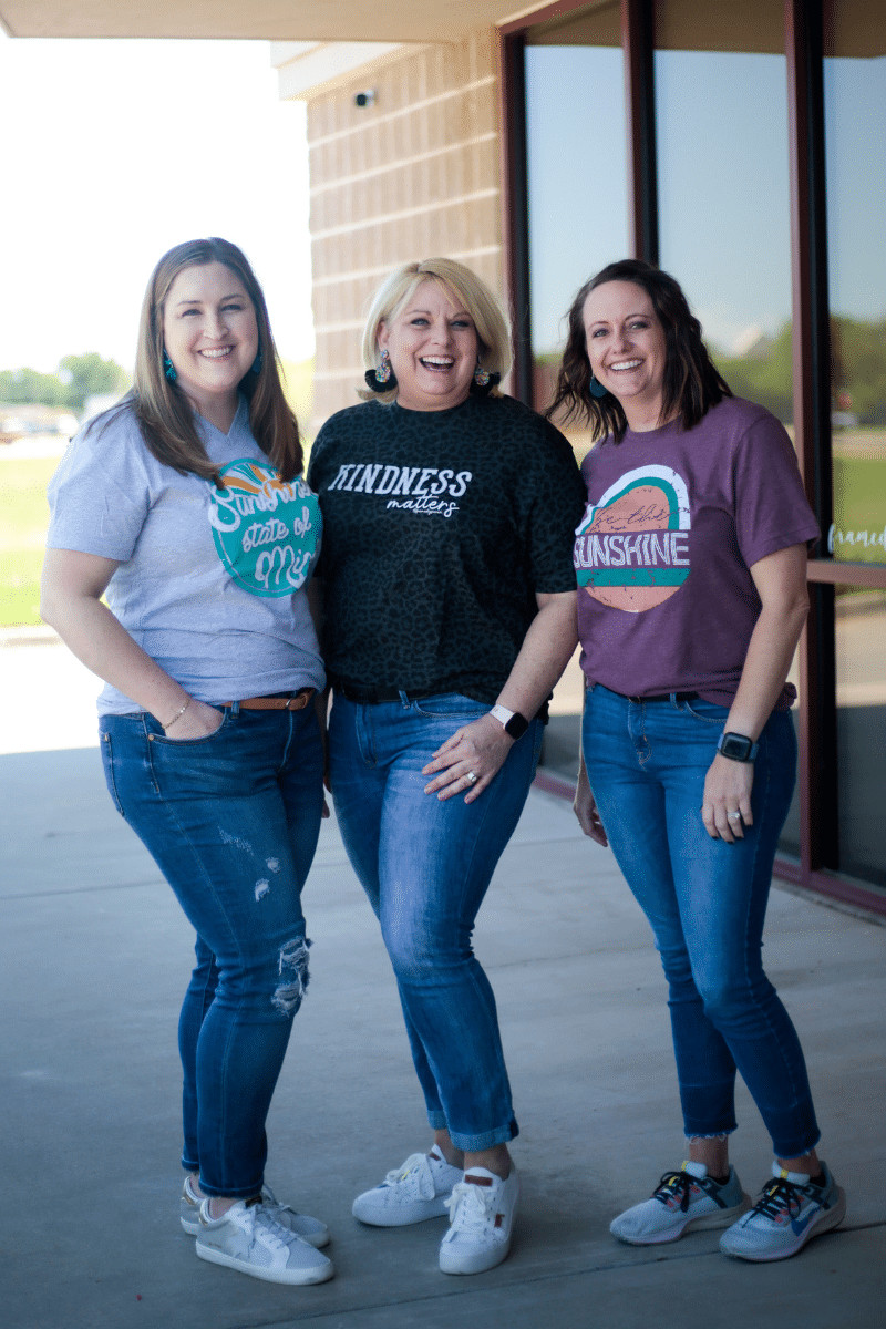 3 Women in Graphic T-Shirts and Jeans standing on a a sidewalk outside