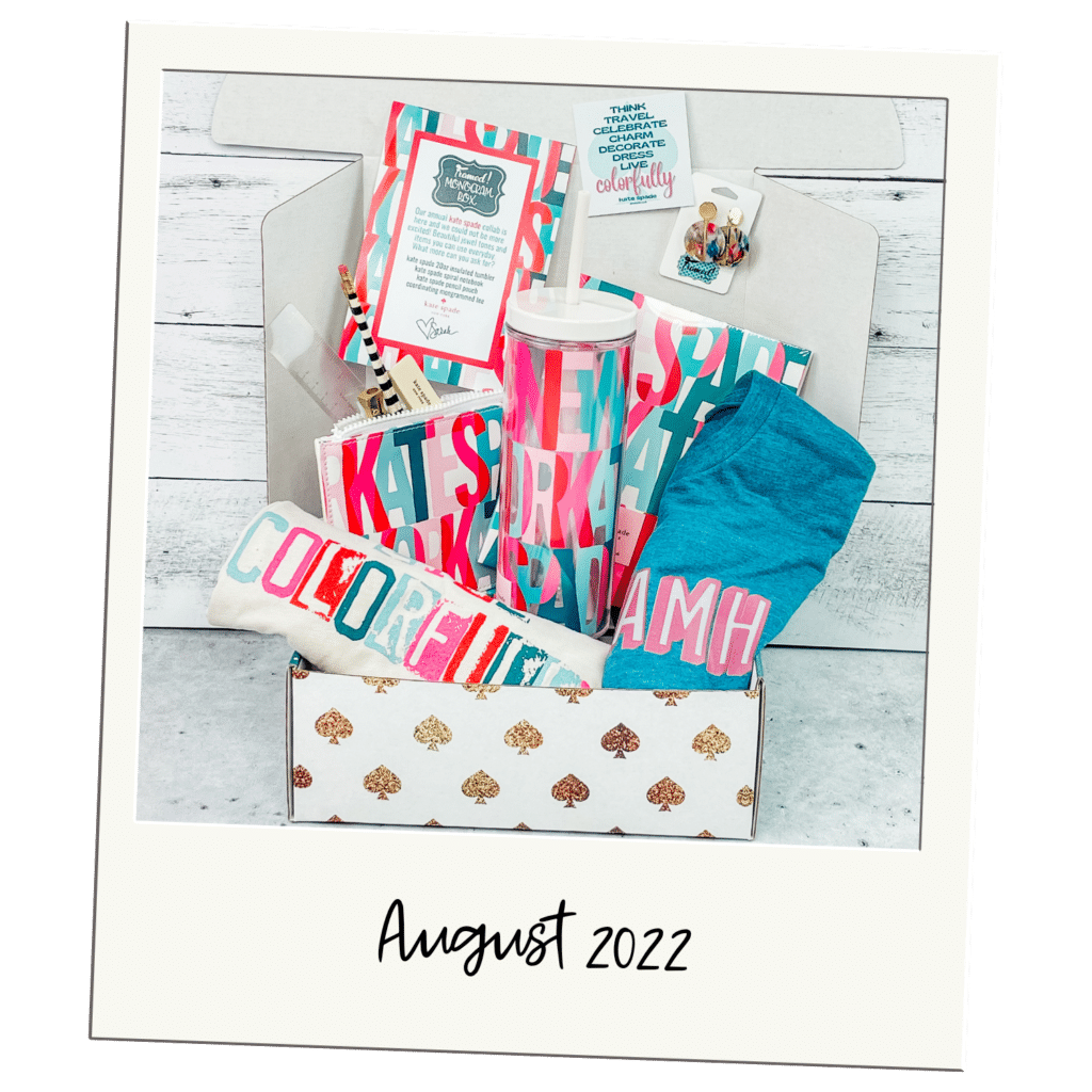 Polaroid picture of a Monogram Box open and displaying Kate Spade Tumbler and notebook, A monogramed blue tshirt, white tshirt with colorful print, and accessories. "August 2022"