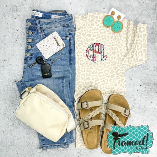 ivory leopard print t-shirt with a colorful monogram on the top right corner styled with ivory belt bag, jeans, neutral sandals, and turquoise jute earrings
