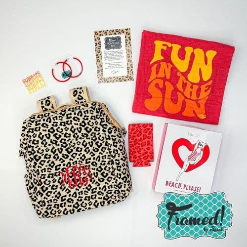 July 2023 Ultimate Monogram Box contents laid out on a white surface. Content include: Leopard backpack with red monogram, red "Fun in the Sun" t-shirt, red hoop earrings, red can coozie, read heart floaty in its packaging.