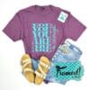 purple tee with "You Are Enough" written in teal styled with ivory sandals, jeans, teal hoop earrings