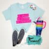 light blue "Be Bold, Be Strong, Be Fearless" text highlighted in hot pink, styled with white jeans, navy sneakers, colorful earrings, and navy striped tumbler