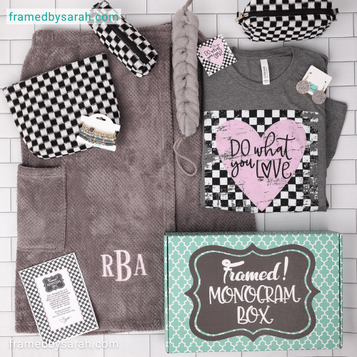 April 2025_Monogram Box and T-Shirt Club displayed on a white time surface near a turquoise box. Contents include: Monogrammed Gray Bath Towel Wrap, black and white checkered cosmetic bag set, gray long loofa scrub, gray t-shirt with "dow what your love" heart graphic, matching earrings and beaded bracelet stack.