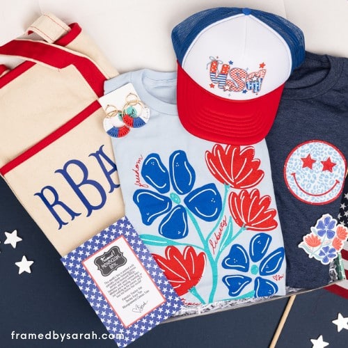 June 2025_Monogram Box and T-Shirt Club displayed inside an open turquoise box. Contents include: light blue patriotic floral tee, navy smily face tee, monogrammed tote bag, red white and blue hoop earrings, and USA trucker hat