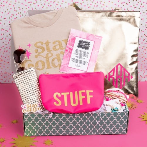 August 2025_Monogram Box displaying all the contents. Contents include: Stay Golden tan tee, sunglasses with gold case, pink and gold bracelet stack, gold monogrammed tote, hot pink "stuff" zipper pouch, and gold earrings.png