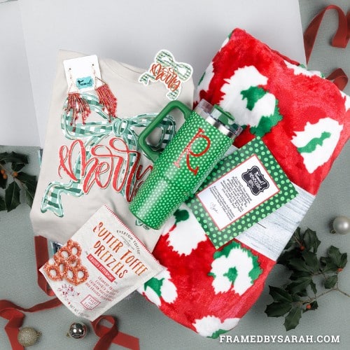 November 2025_Monogram Box displaying all the contents. Contents include: Monogrammed green tumbler, large cozy red and green leopard blanket, butter toffee pretzels, "merry" bow graphic tee, and red beaded earrings