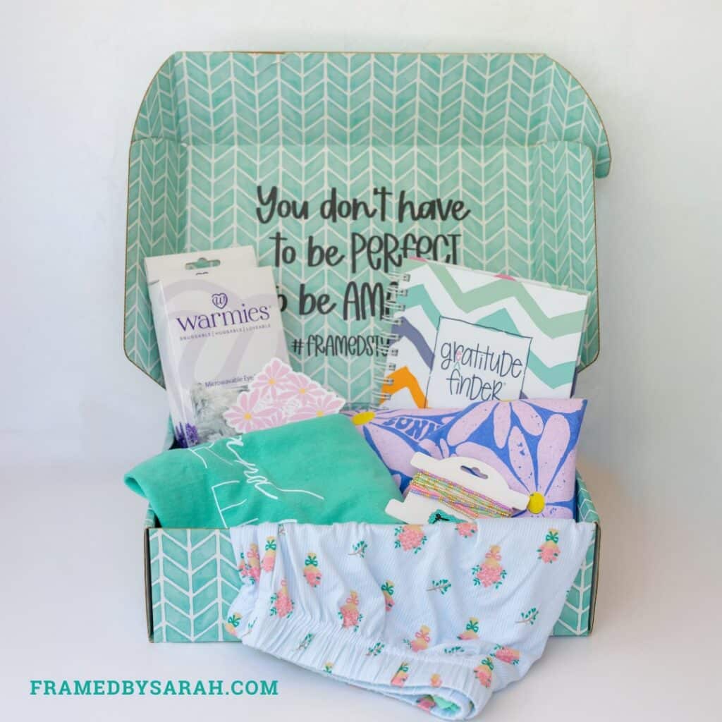 floral pajama shorts, teal t-shirt, blue t-shirt, eye mask, bracelet stack, and journal displayed in a teal subscription box