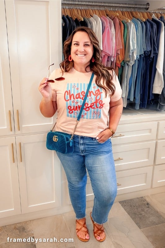 Sarah wearing the "chasing sunsets" tshirt styled with jeans, a teal purse, tan sandals and glasses