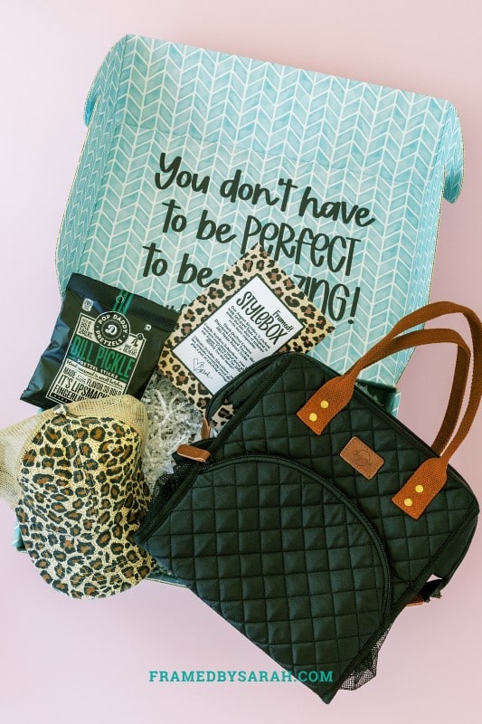 teal box open and displaying black quilted cooler tote bag, leopard print trucker hat, and a bag of pretzels