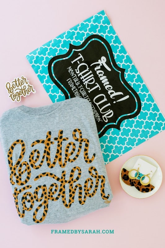 T-Shirt Club teal bag with a folded gray "better together" t-shirt, better together sticker, and leopard earrings