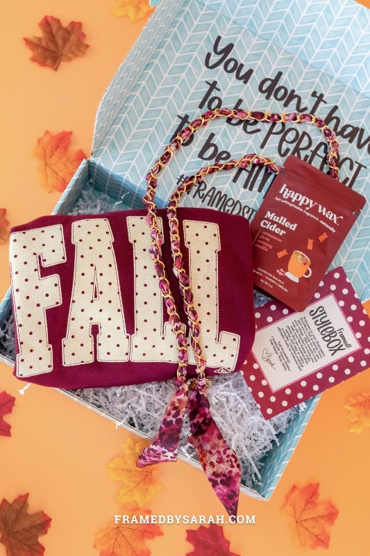 teal Framed Style Box open displaying the contents which include, maroon "fall" sweatshirt, scarf phone chain, cider wax melts, and print insert.