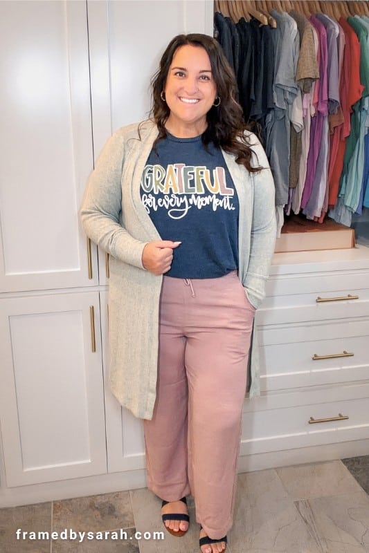 Sarah Williams wearing the navy "Grateful for Every Moment" t-shirt styled with mauve linen pants. gray long cardigan, and navy sandals