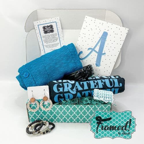 October 2023 Ultimate Monogram Box open with contents displayed. Content include: "Grateful Grateful Grateful Heart" black tshirt, blue cardigan, hoop earrings, bracelet stack, leather headband, monogram print